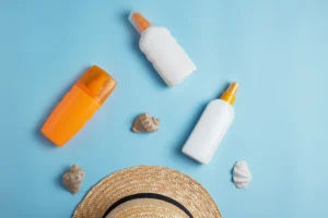 Różne kosmetyki na lato, obok muszelek i kapelusza plażowego
